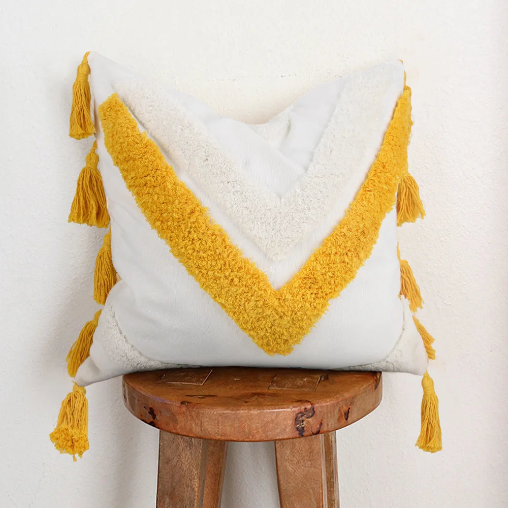 Coussin blanc moelleux avec des franges jaunes décoratives, reposant sur un tabouret en bois rustique.