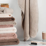 Pile de serviettes douces et moelleuses dans des tons de beige et de marron, une brosse en bois sur le côté, symbolisant la douceur et la propreté dans une salle de bain.