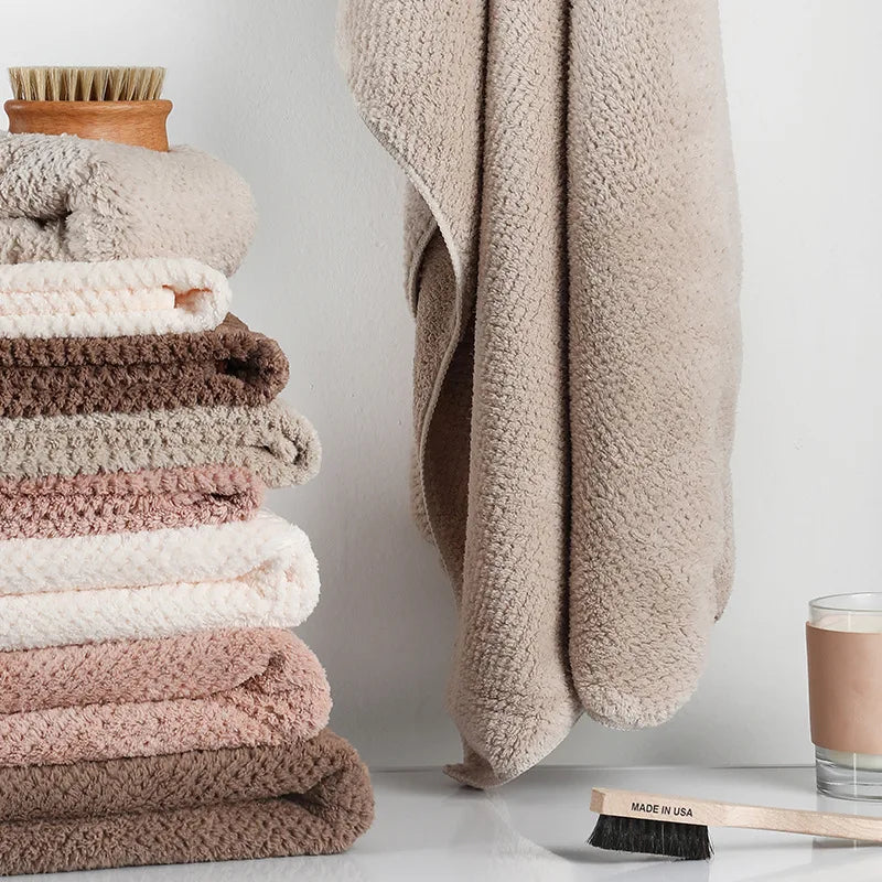 Pile de serviettes douces et moelleuses dans des tons de beige et de marron, une brosse en bois sur le côté, symbolisant la douceur et la propreté dans une salle de bain.