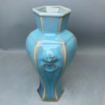 Un vase décoratif hexagonal en céramique de couleur bleu turquoise avec des reflets dorés.