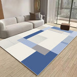 Tapis géométrique aux teintes bleues et grises posé dans un salon moderne avec un canapé blanc et un parquet en bois.