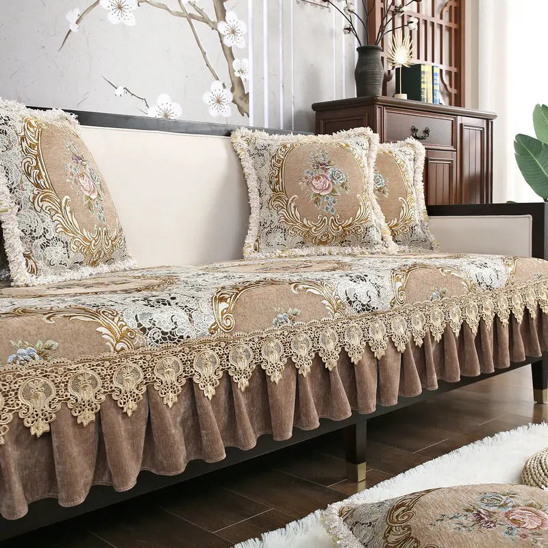 Cette image représente un canapé d'intérieur élégant et luxueux, avec des coussins et une couverture ornés de motifs floraux dorés sur un fond beige. Le canapé est placé dans un intérieur moderne avec des éléments décoratifs en bois sombre.