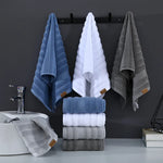 Serviettes de bain de couleurs bleu, blanc et gris suspendues sur une barre murale noire, avec des piles de serviettes assorties près du lavabo.