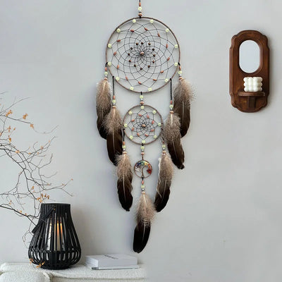 Cette image montre un capteur de rêves décoratif suspendu au mur, avec de multiples anneaux tressés et ornés de plumes marron.
