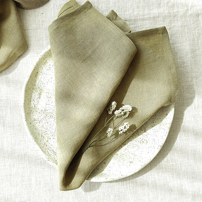 Serviettes de table en lin vert olive ornées de petites fleurs blanches sur un fond texturé.