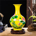 Un vase décoratif en céramique de couleur jaune vif, orné de motifs floraux colorés représentant des lotus et autres plantes aquatiques, posé sur un socle en bois.