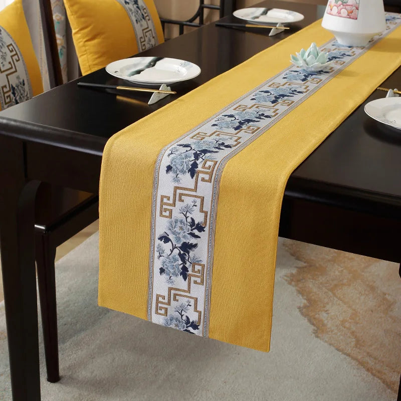 Élégant chemin de table en textile jaune avec motifs graphiques bleus et dorés, disposé sur une table en bois foncé.
