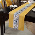 Élégant chemin de table en textile jaune avec motifs graphiques bleus et dorés, disposé sur une table en bois foncé.