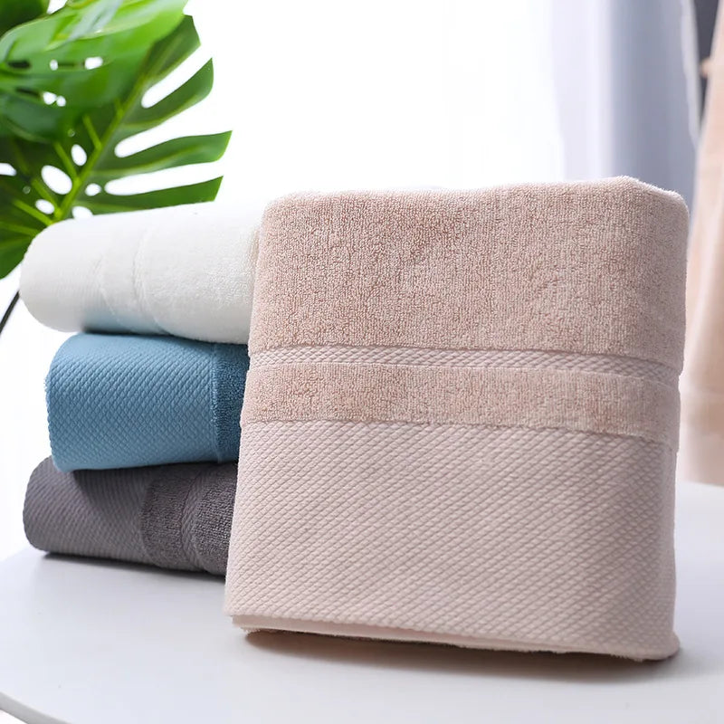 Pile de serviettes douces de différentes couleurs reposant sur une surface blanche avec des feuilles vertes en arrière-plan.
