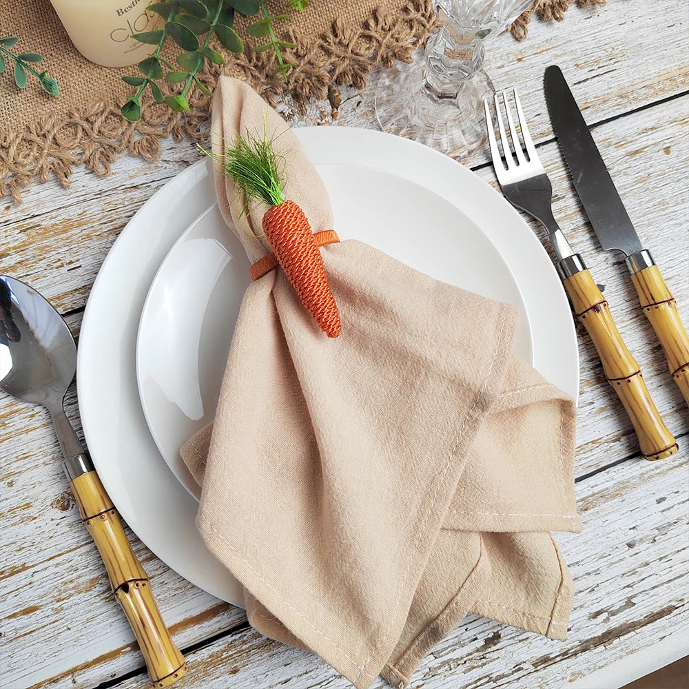 Assiette blanche avec une serviette beige enroulée autour d'une carotte en forme de fleur, posée sur un fond de bois clair avec des couverts en bambou.