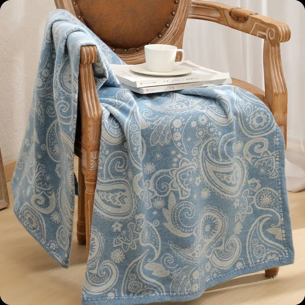 Élégante couverture en coton bleu orné de motifs paisley, posée sur un fauteuil vintage en bois, accompagnée d'une tasse de café sur une pile de disques vinyl.