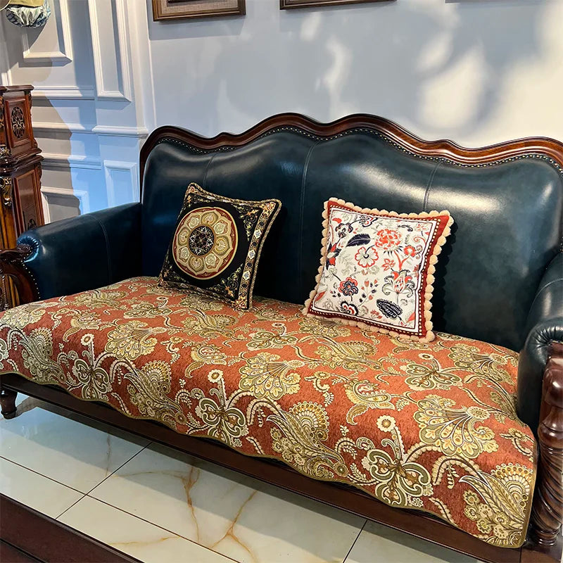 Un sofa en cuir noir avec des coussins décoratifs ornés de motifs floraux aux couleurs chaudes, placé sur un sol carrelé.