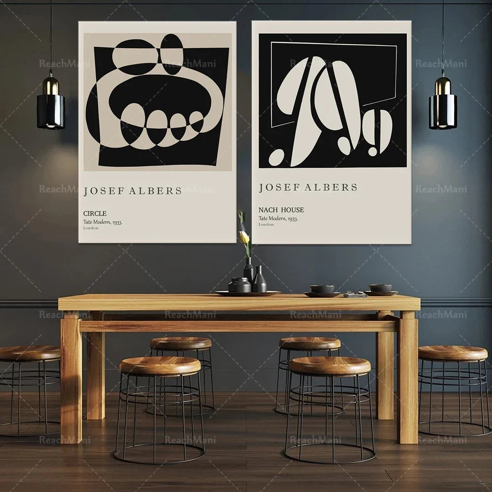 Deux affiches d'art abstraites de Josef Albers encadrant une table en bois avec des tabourets, créant une ambiance moderne et épurée dans cette salle à manger.