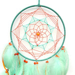 Un magnifique capteur de rêves avec un motif géométrique en spirale coloré, composé de fils rouges et vert menthe, surmonté d'une pierre orange et entouré de jolies plumes teintées.