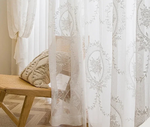 Détail du voilage blanc esprit bord de mer avec broderies florales dans un intérieur chaleureux