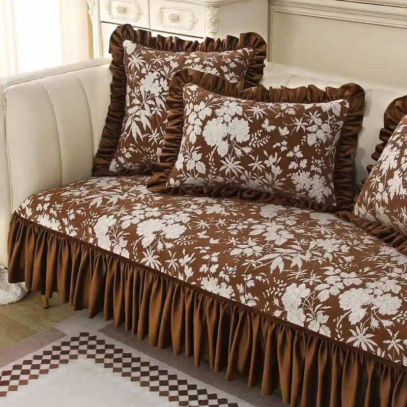 Couvre-lit et oreillers vintage ornés de motifs floraux dans des tons de marron et de blanc, placés sur un canapé avec des accents de couleur grise et blanche.