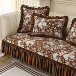 Couvre-lit et oreillers vintage ornés de motifs floraux dans des tons de marron et de blanc, placés sur un canapé avec des accents de couleur grise et blanche.