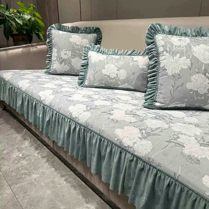 Housse de canapé en tissu fleuri de couleur vert menthe avec volants décoratifs, créant une ambiance élégante et chaleureuse dans la pièce.