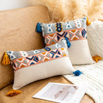 Coussins décoratifs géométriques multicolores sur un canapé beige, avec des pompons et des tassels bleus et jaunes, entourant une photographie.