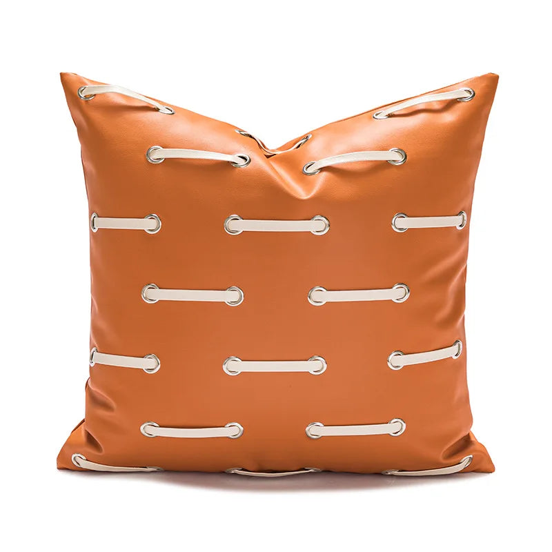 Coussin décoratif carré en cuir synthétique orange orné de coutures et d'anneaux métalliques.