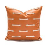 Coussin décoratif carré en cuir synthétique orange orné de coutures et d'anneaux métalliques.