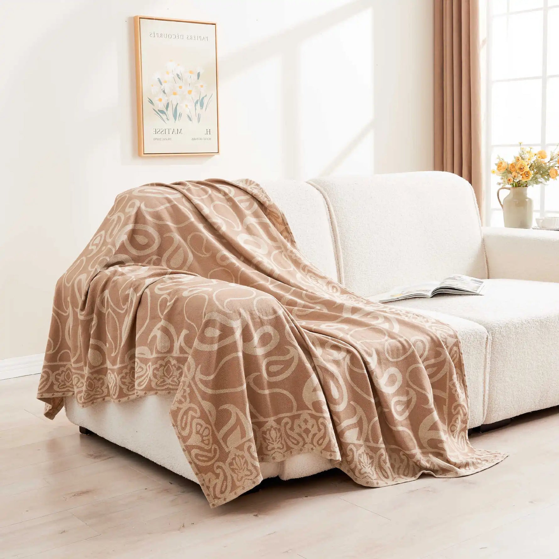 Couverture douillette en tissus motif damassé sur un canapé, avec un vase de fleurs dans le coin et un cadre décoratif sur le mur.