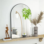 Le miroir arrondi en métal noir avec une structure en laiton doré crée un bel accent décoratif, accompagné de plantes vertes épanouies et d'accessoires de style contemporain sur une étagère en bois.