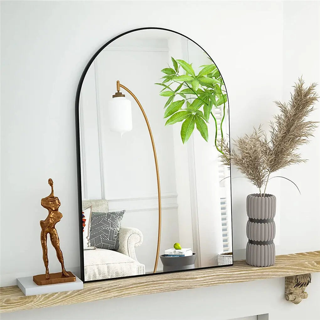 Le miroir arrondi en métal noir avec une structure en laiton doré crée un bel accent décoratif, accompagné de plantes vertes épanouies et d'accessoires de style contemporain sur une étagère en bois.