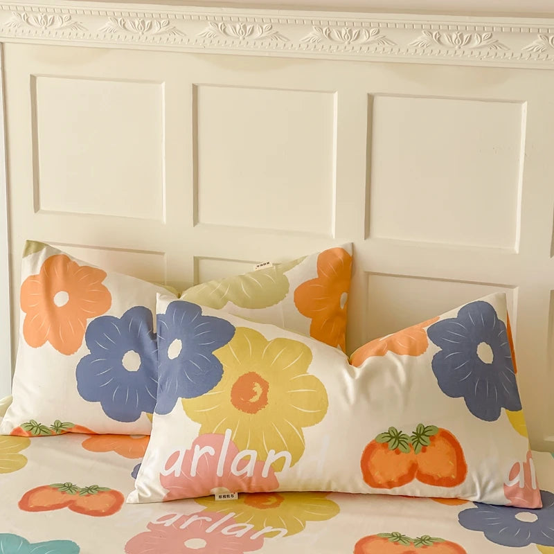 Cet ameublement de chambre présente un motif floral coloré avec des fleurs géométriques aux nuances de jaune, orange et bleu sur un fond clair. La décoration comporte des coussins et une housse de couette assortis.