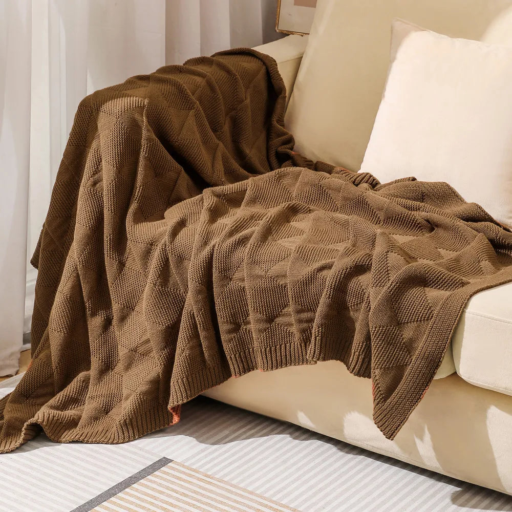 Une couverture tricotée en laine de couleur brun foncé, posée sur un canapé, offrant un aspect douillet et confortable dans l'espace.