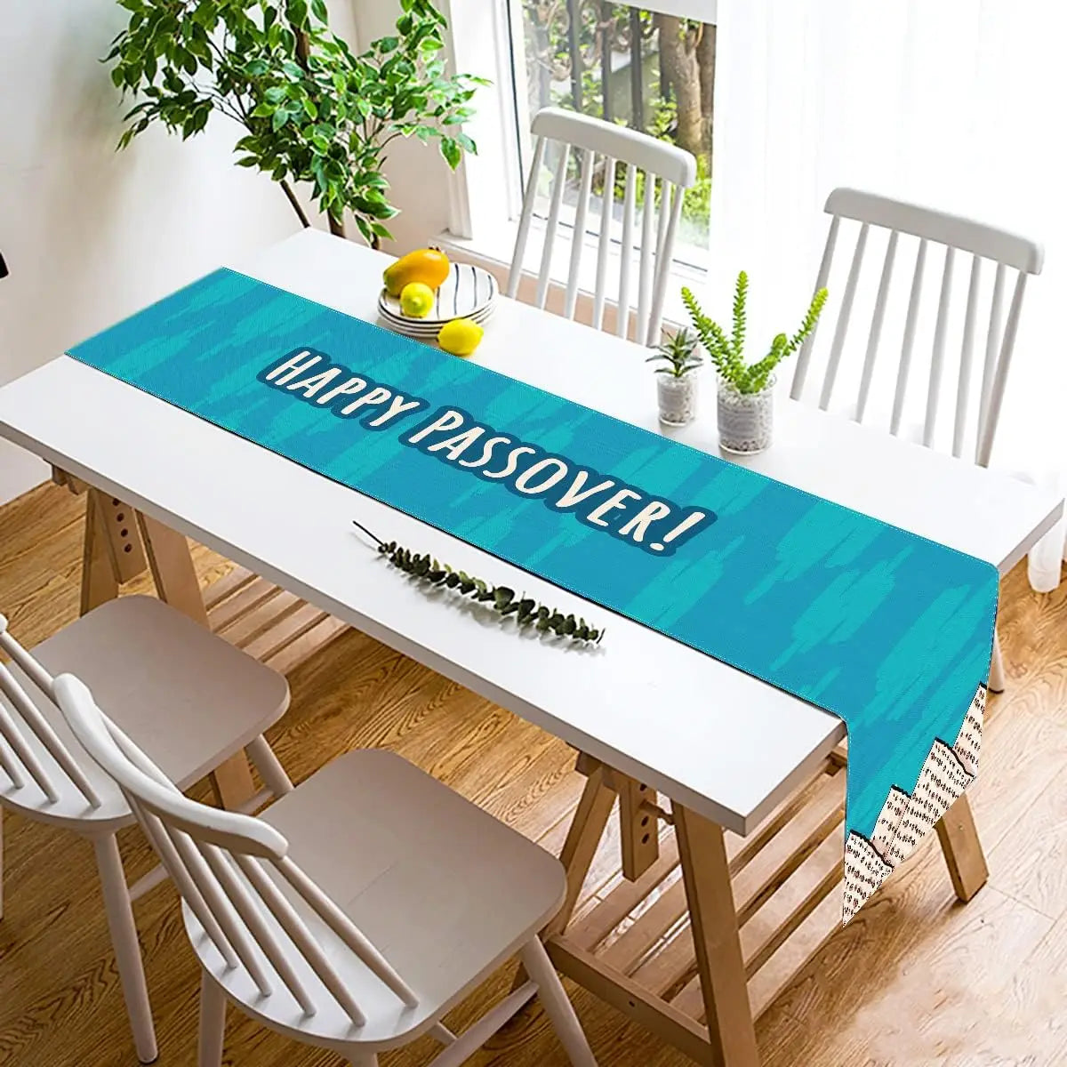 Une table de salle à manger avec des chaises blanches, une plante verte et un plateau de fruits sur le dessus, décorée d'un joyeux message sur un chemin de table.