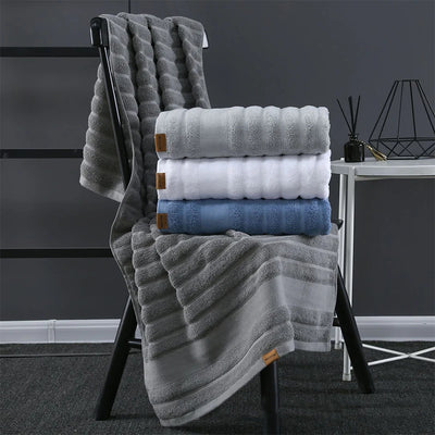 Une pile de serviettes de bain grises, blanches et bleues, pliées avec soin sur un portant noir, créant une composition élégante et minimale dans un intérieur sombre.