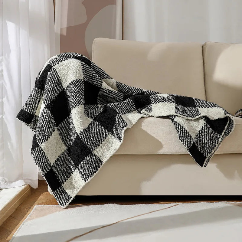 Une couverture à carreaux noir et blanc apporte une touche de style rustique et confortable sur le canapé beige.