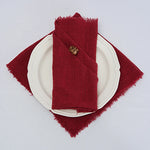 Serviette rouge à franges posée sur une assiette blanche.