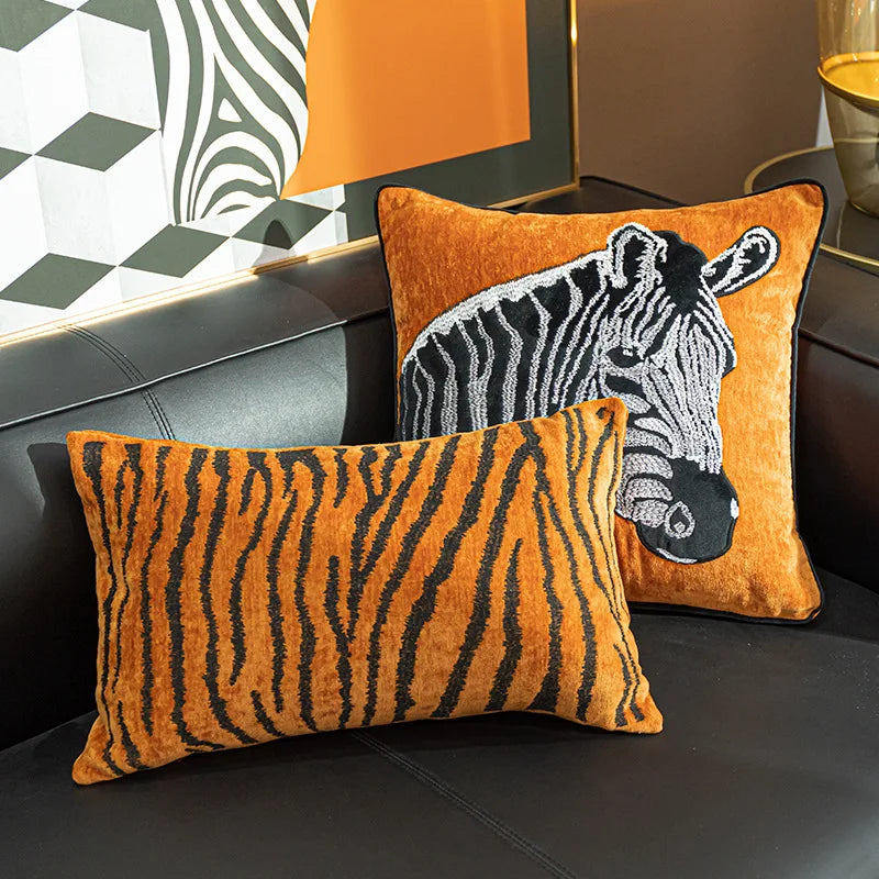 Deux coussins en velours côtelé orange orné d'impressions de zèbres posés sur un canapé sombre.