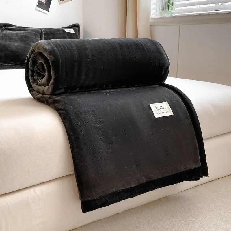 Une couverture en peluche noire, douce et confortable, posée sur un canapé blanc dans un intérieur moderne.