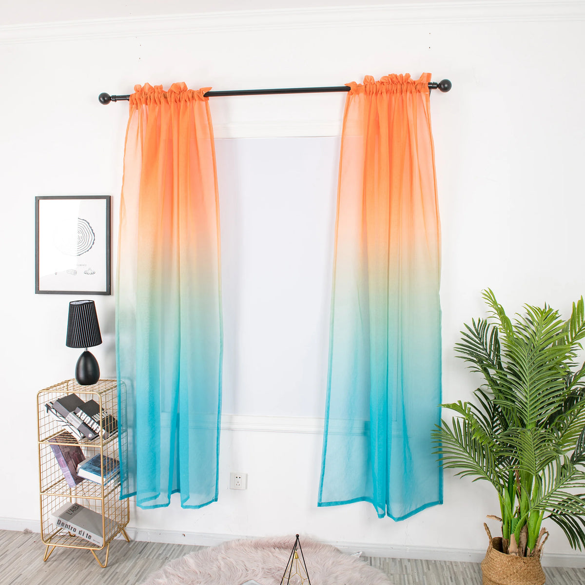 Voilage dégradé orange et bleu ciel suspendu à une tringle noire, dans une pièce lumineuse avec plantes vertes et tapis moelleux.