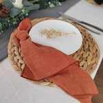 Une assiette blanche avec une broderie florale sur un napperon en fibres tressées, accompagné d'un linge de table orange.