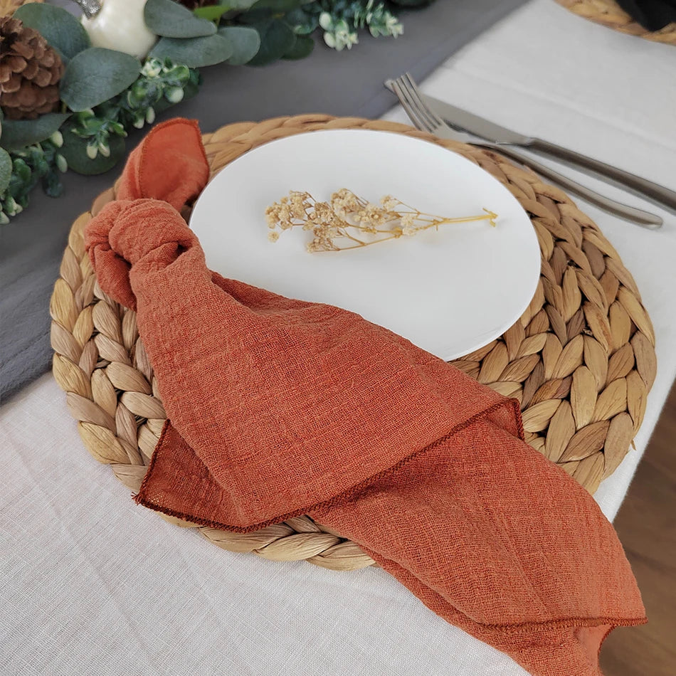 Une assiette blanche avec un motif doré posée sur un napperon tressé en fibres naturelles, accompagnée d'un linge de table en coton rouille.