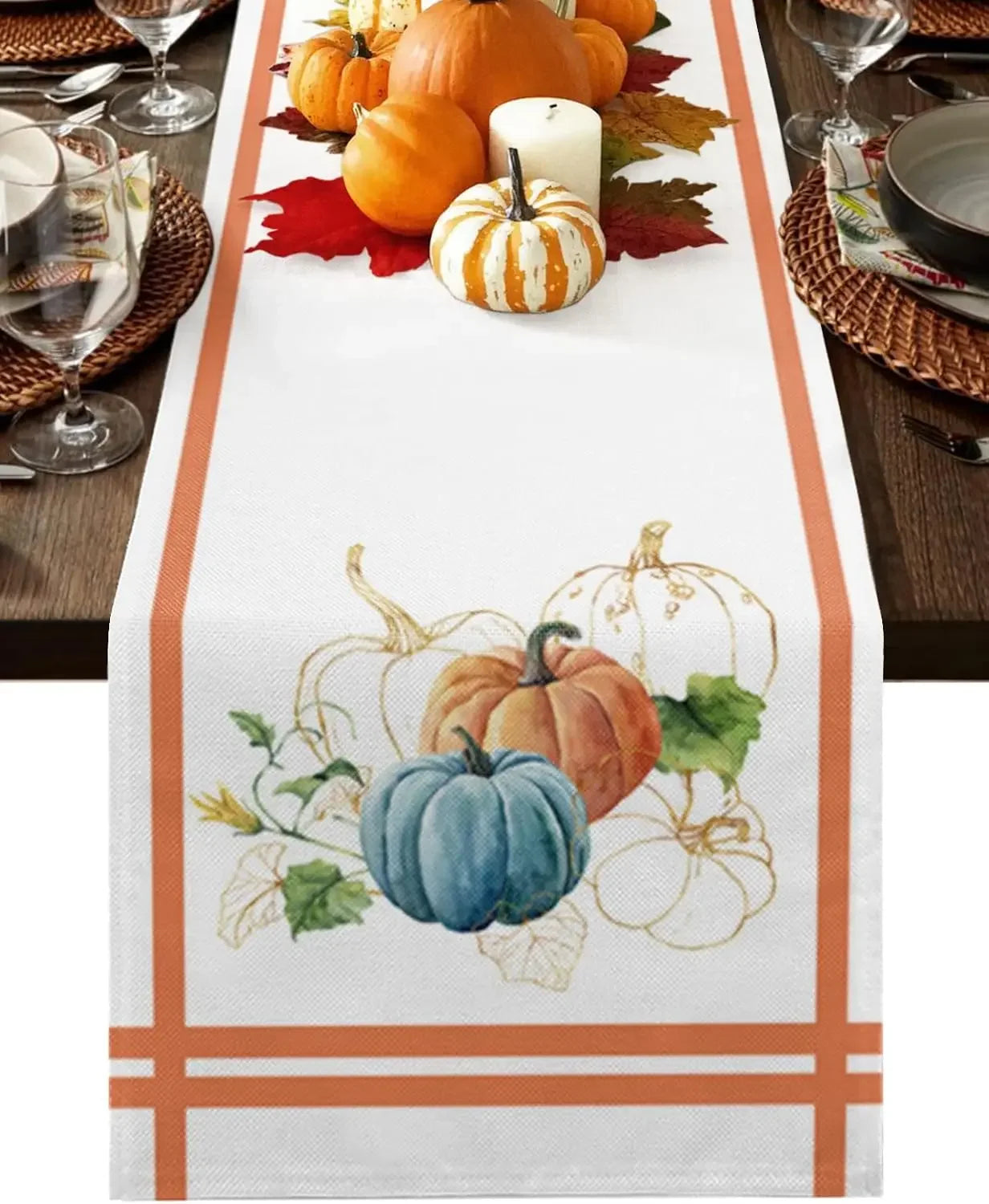 Une nappe de table blanche avec des dessins de citrouilles d'automne dans des tons orange et bleu, entourés de feuilles rouges, pour créer une décoration automnale élégante.