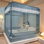 L'image montre un lit avec un cadre élégant en métal gris, décoré de rideaux bleus et blancs avec des ornements délicats. Une personne est assise sur le lit, en train de lire quelque chose sur un appareil portable.