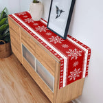 Le chemin de table rouge avec des motifs de flocons de neige apporte une touche festive et hivernale à cette commode en bois, créant une atmosphère chaleureuse et accueillante dans la pièce.