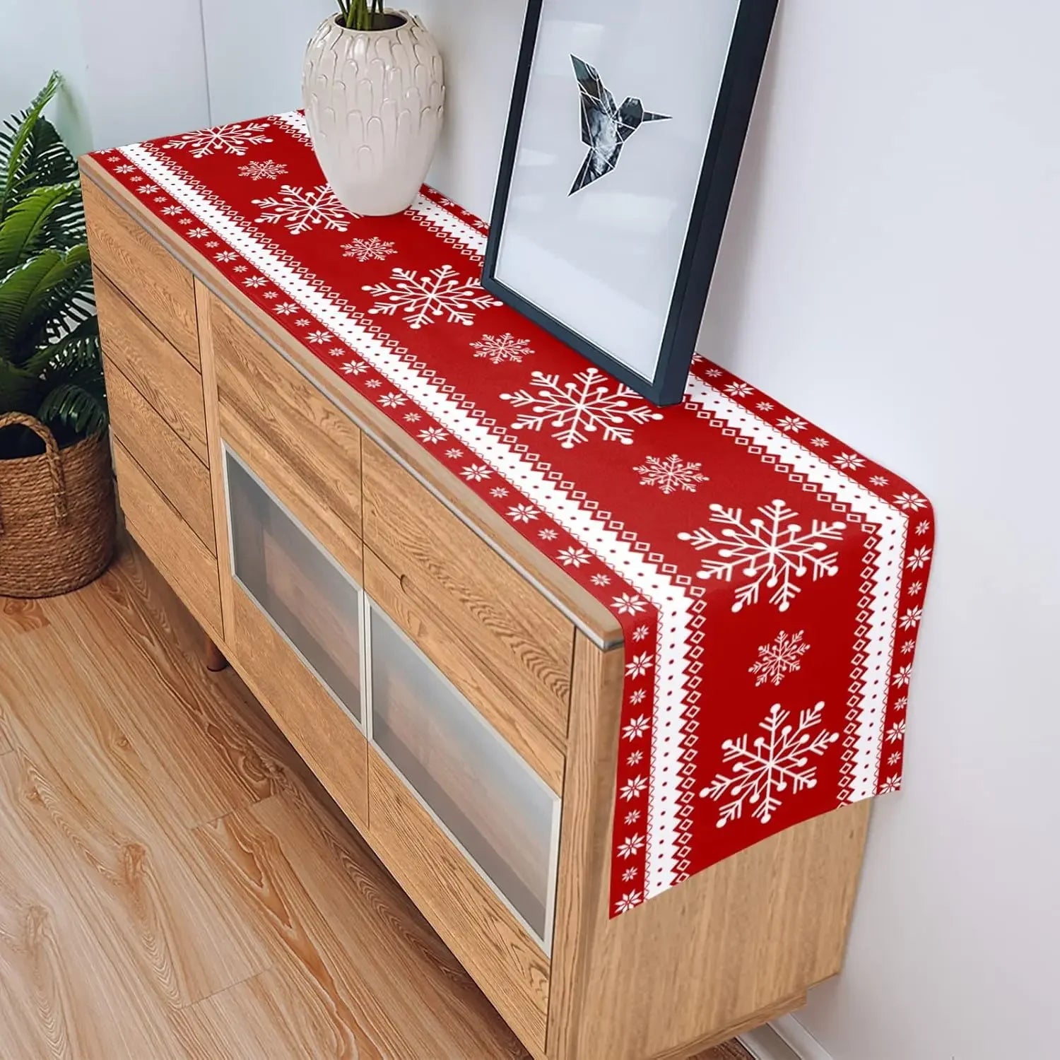 Le chemin de table rouge avec des motifs de flocons de neige apporte une touche festive et hivernale à cette commode en bois, créant une atmosphère chaleureuse et accueillante dans la pièce.