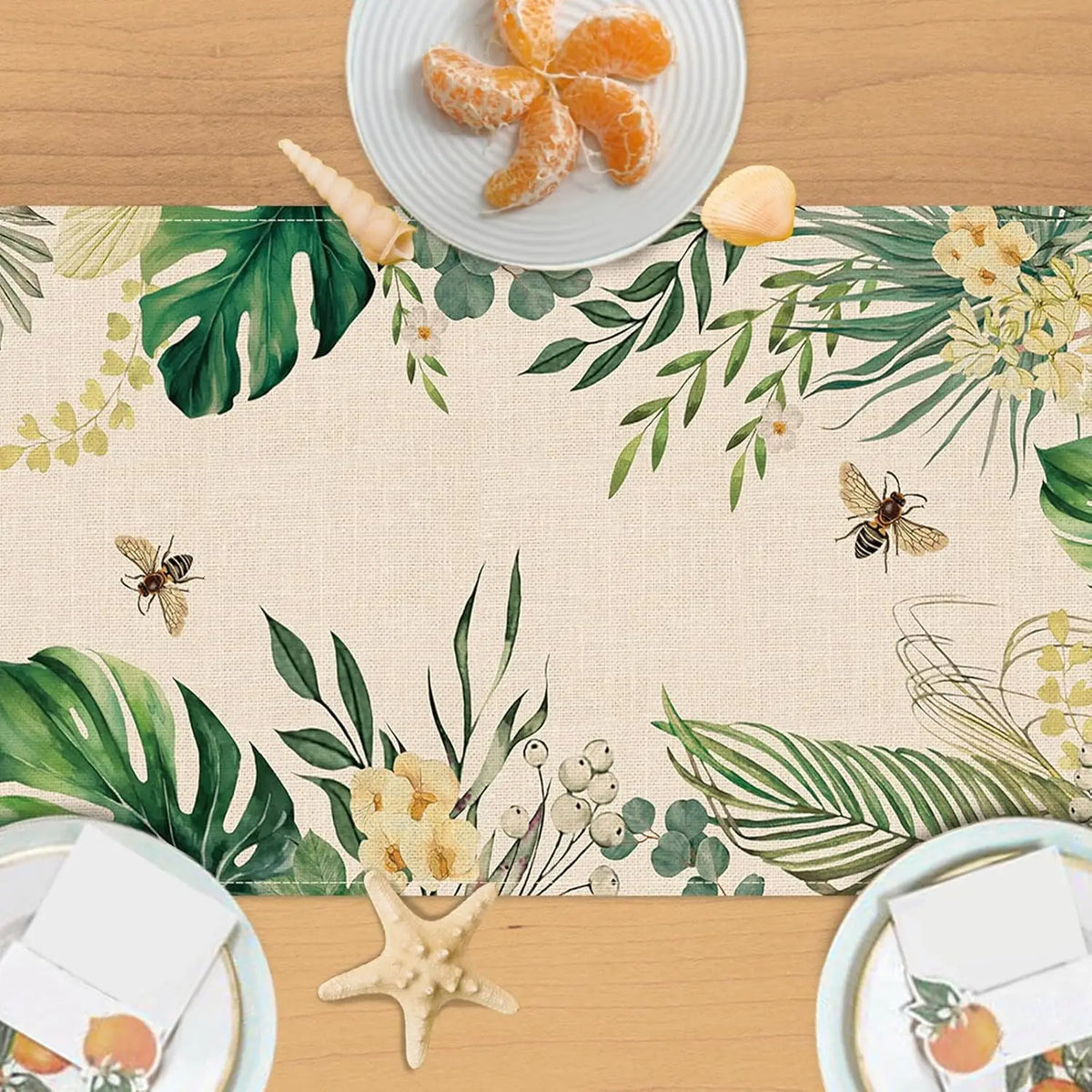 Une nappe colorée avec des motifs de feuilles tropicales et de fleurs, entourant des assiettes avec des oranges et des étoiles de mer, évoquant une atmosphère estivale et exotique.