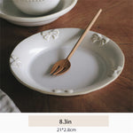 Assiette blanche ornée de motifs floraux avec un ustensile en bois posé dessus, sur une surface en bois foncé.