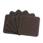 Des sous-verres carrés en cuir marron avec coutures blanches, empilés les uns sur les autres.