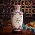 Un vase décoratif en céramique blanche avec des motifs colorés floraux et géométriques, posé sur un support en bois, entouré d'autres objets ethniques.