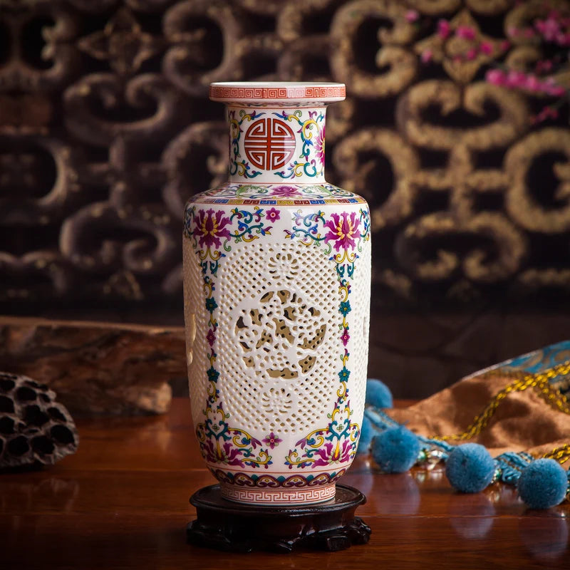 Un vase décoratif en céramique blanche avec des motifs colorés floraux et géométriques, posé sur un support en bois, entouré d'autres objets ethniques.