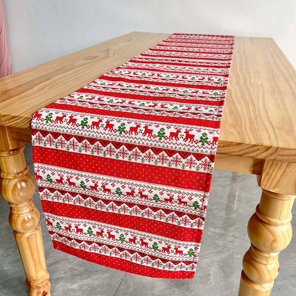 Cette image montre un chemin de table de Noël orné de motifs rouges et verts, avec des rennes et des flocons de neige répétés sur le tissu.