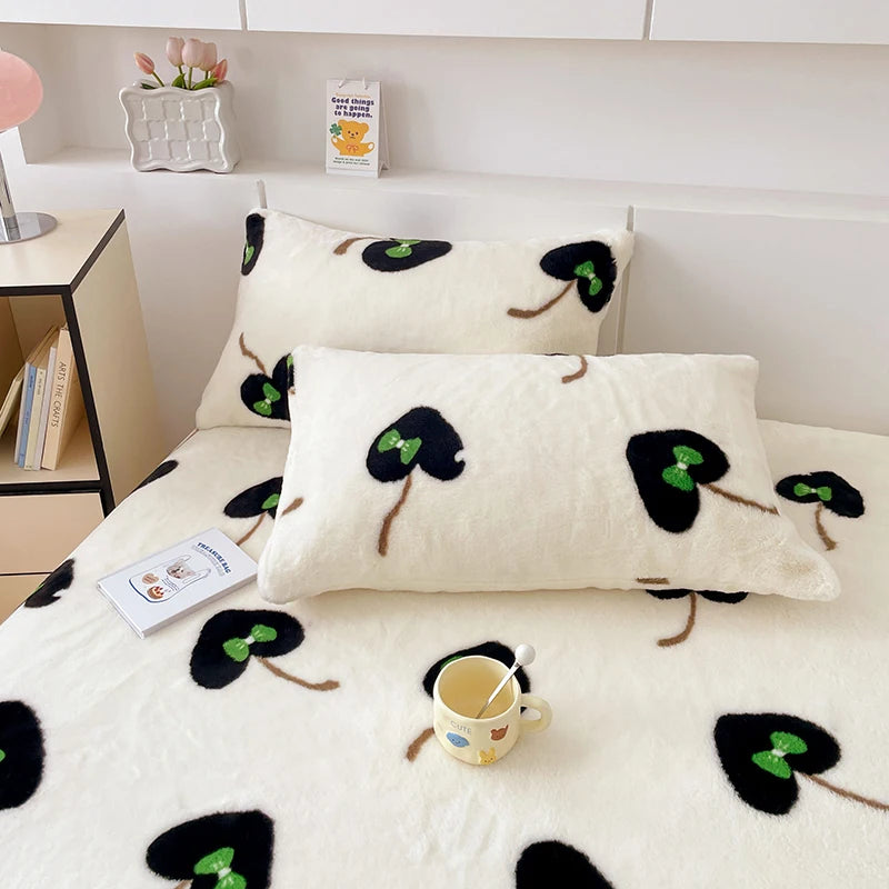 Ensemble de literie moelleux et douillet avec des motifs de trèfles verts sur un fond blanc, décoré d'une tasse de boisson chaude et d'un accessoire avec un ours en peluche, créant une ambiance chaleureuse et confortable.